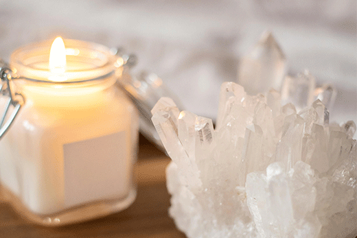 Close-up of a white candle burning next to a clear quartz crystal cluster